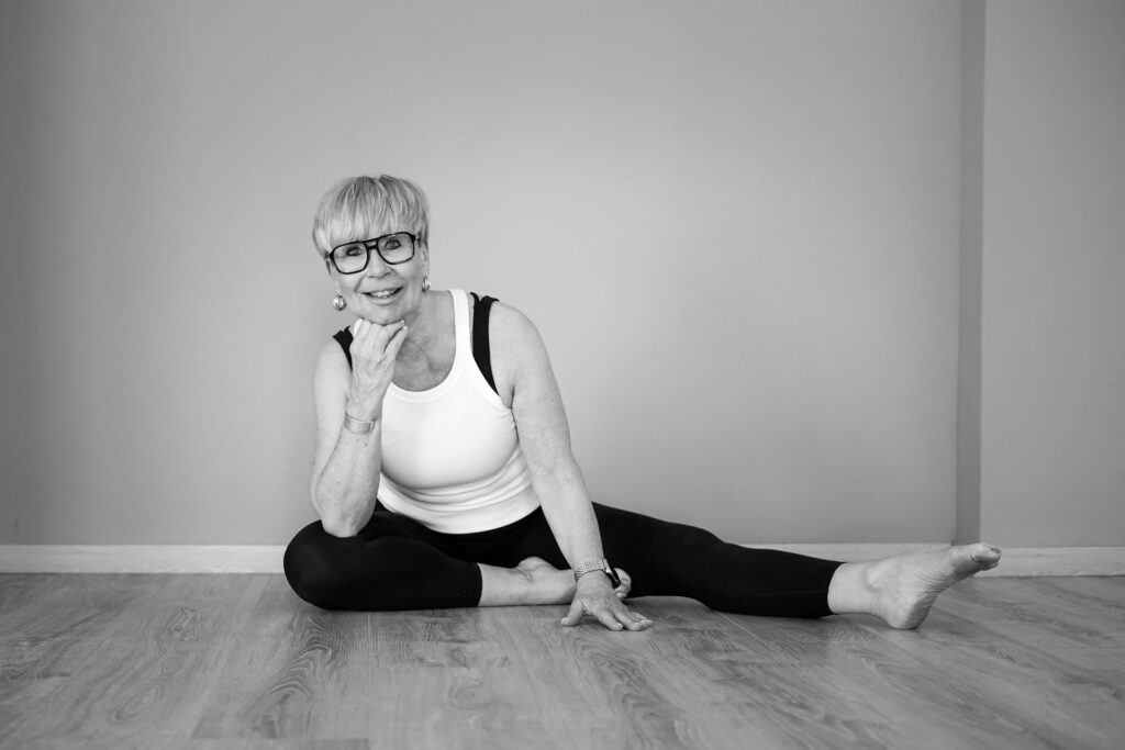 Karin Möller sitzt im Grätschsitz auf dem Studioboden, die Hand am Kinn