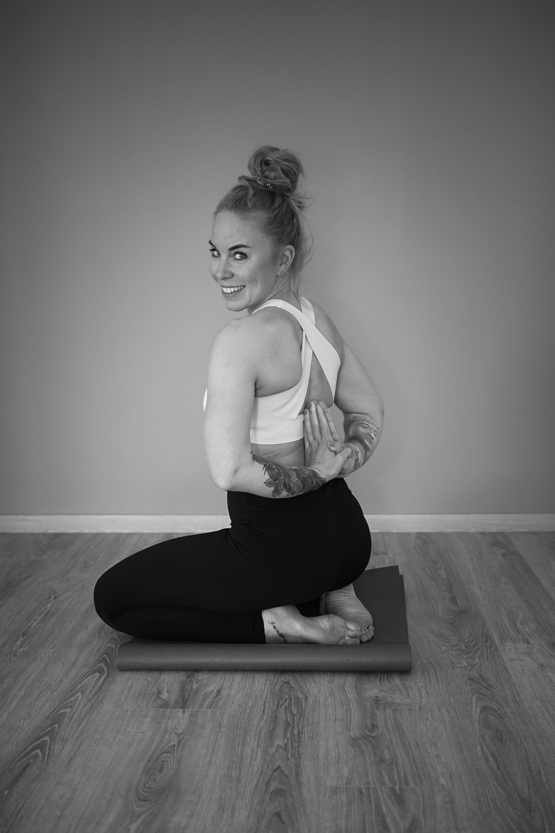 Rabea kniet auf einem Yogablock, die Hände hinter dem Rücken gefaltet, und blickt über die Schulter